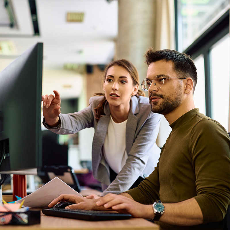 Young IT professional working at desk with colleagues in background