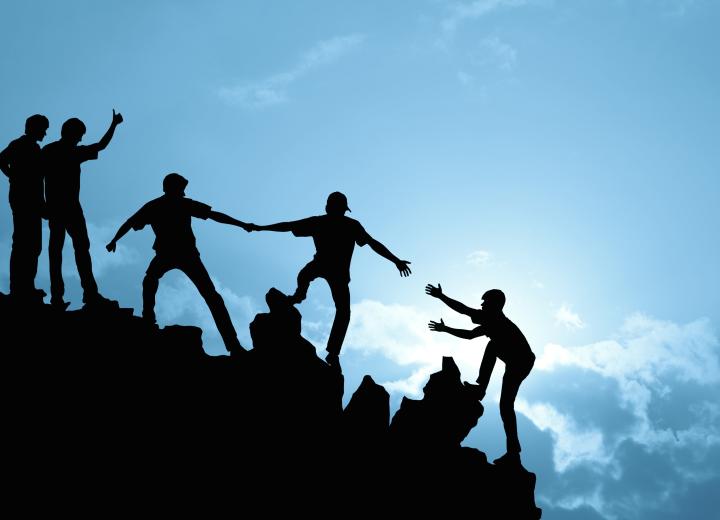 Group of people helping each other whilst climbing up rock